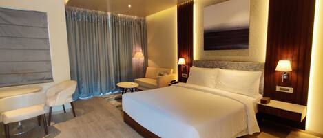 A modern hotel room with a large bed, a desk, a chair, and a small table.