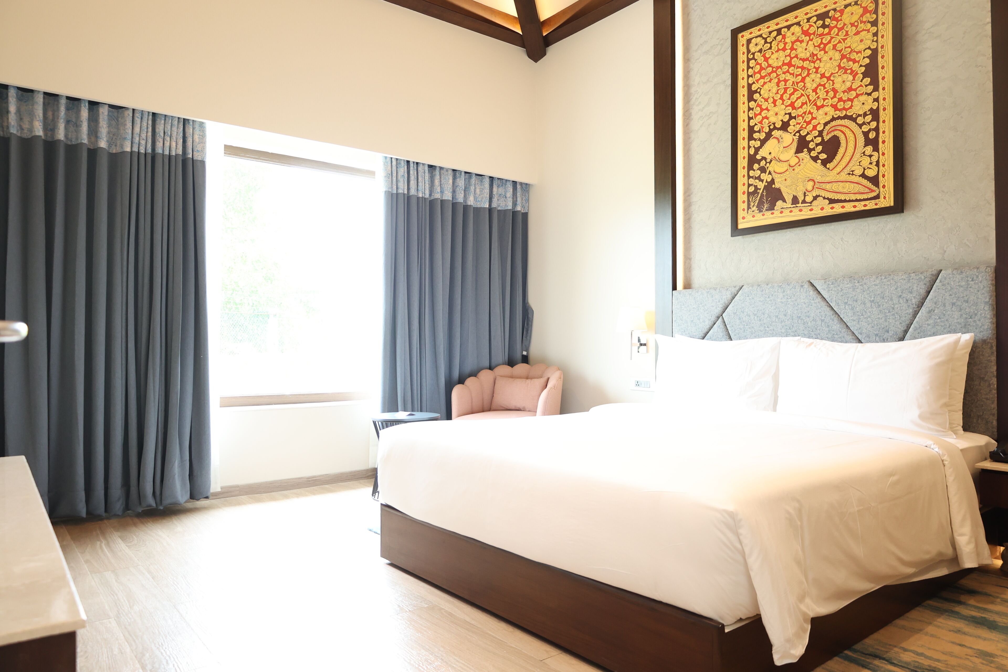 Una habitación de hotel con una cama grande, un escritorio, una silla y un ventanal con cortinas.