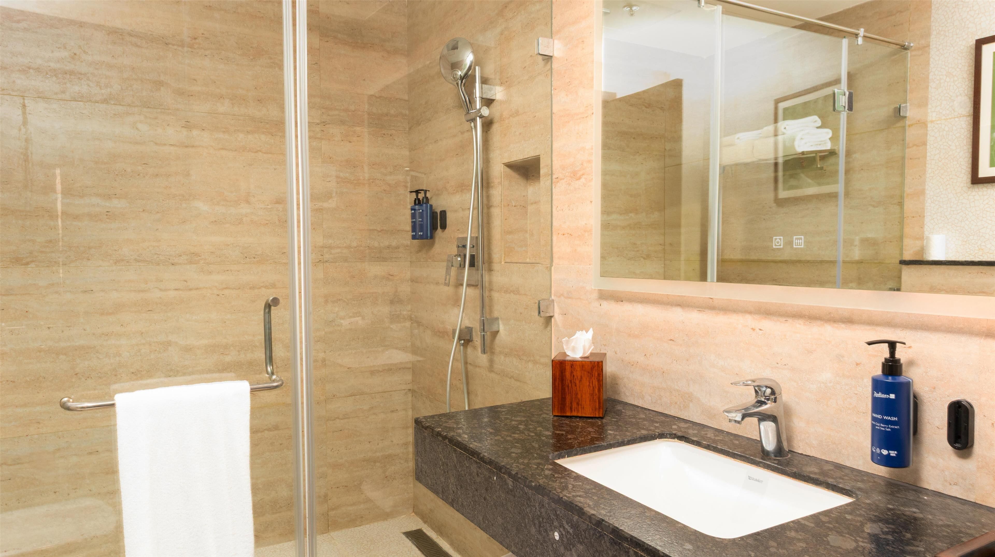 A bathroom with a glass shower enclosure, a sink with a marble countertop, and a mirror above the sink.