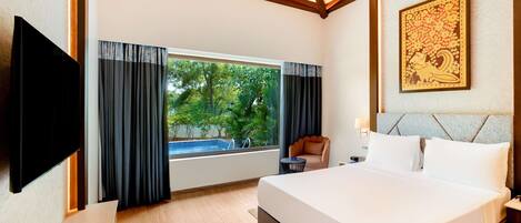 A hotel room with a large bed, a TV mounted on the wall, a window with curtains, a small table, and a chair.