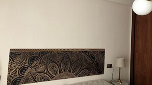 Una habitación de hotel con un gran tapiz decorativo en la pared, una lámpara de noche y una lámpara de techo.