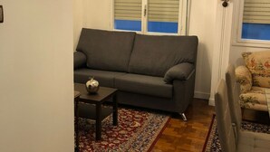 Un salón con un sofá gris, una mesita, un tapiz estampado y una araña.