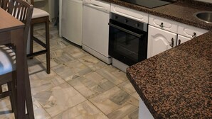 Una cocina con armarios blancos, lavavajillas, horno y encimera de granito.