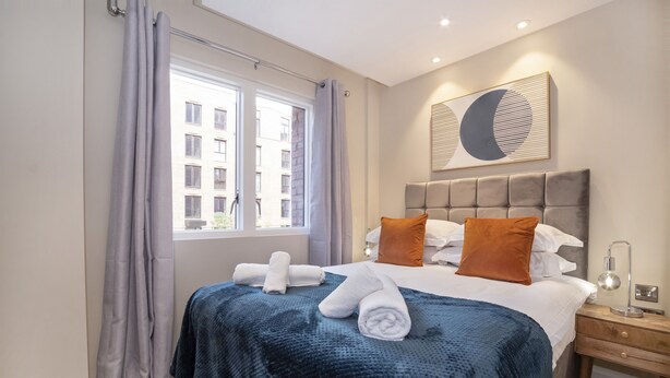 A hotel room with a bed, a nightstand, a lamp, and a window with curtains.