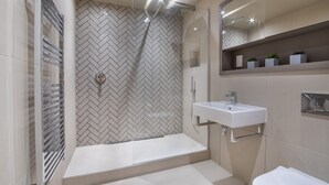 A modern bathroom with a herringbone tile backsplash, a glass shower enclosure, a white sink, and a built-in shelf with plants.