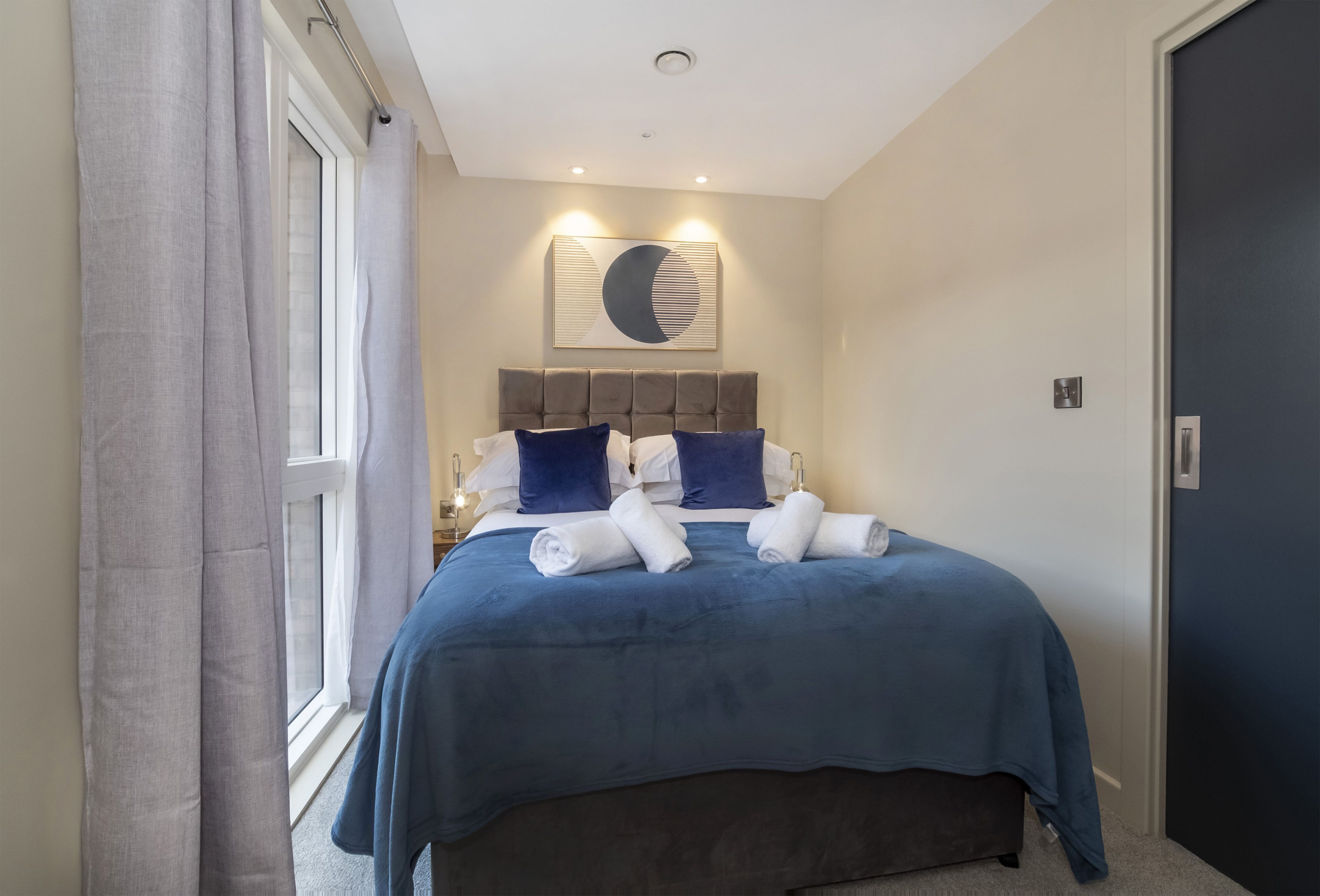A bedroom with a bed, a headboard, a wall-mounted artwork, and a window with curtains.