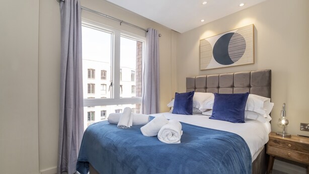 A hotel room with a large bed, a view of buildings outside, and a wall-mounted artwork. - Apartment 28 Hudson Quarter Luxury Apartments - sleeps 4 guests  in 1 bedroom (York)
