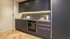 A modern kitchen with dark cabinetry, a built-in oven, and a countertop with a toaster and coffee maker. - Apartment 28 Hudson Quarter Luxury Apartments - sleeps 4 guests  in 1 bedroom (York)