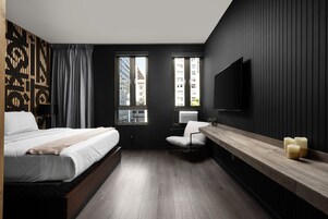 Quarto de hotel moderno com uma cama grande, uma escrivaninha com cadeira, TV fixada na parede e janela com vista para a cidade.