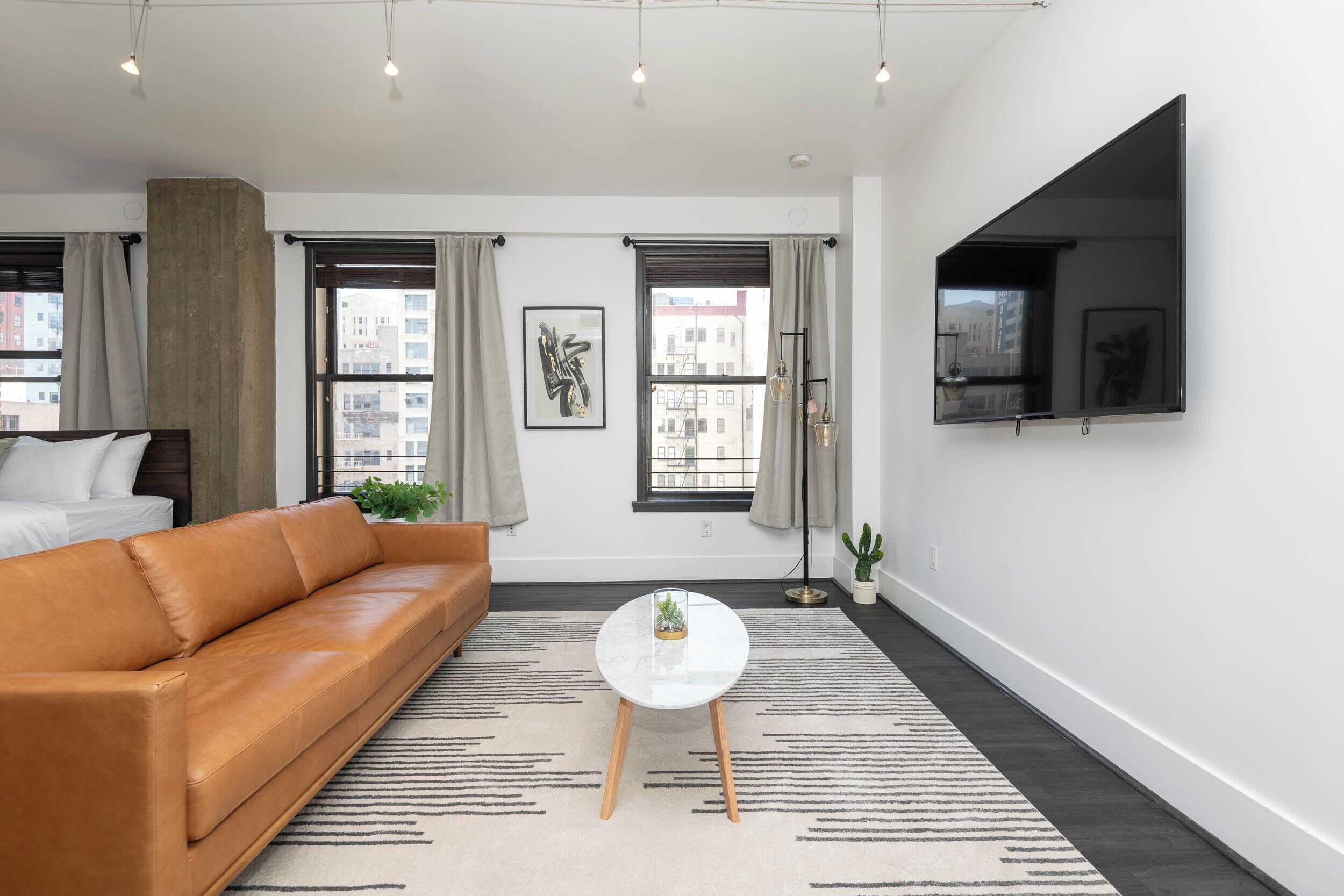 Un salon moderne avec un canapé en cuir, une table ronde blanche et un grand téléviseur à écran plat fixé au mur.