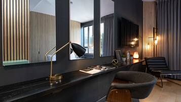 A modern room with a black desk, a chair, a large mirror, and a wall-mounted lamp.