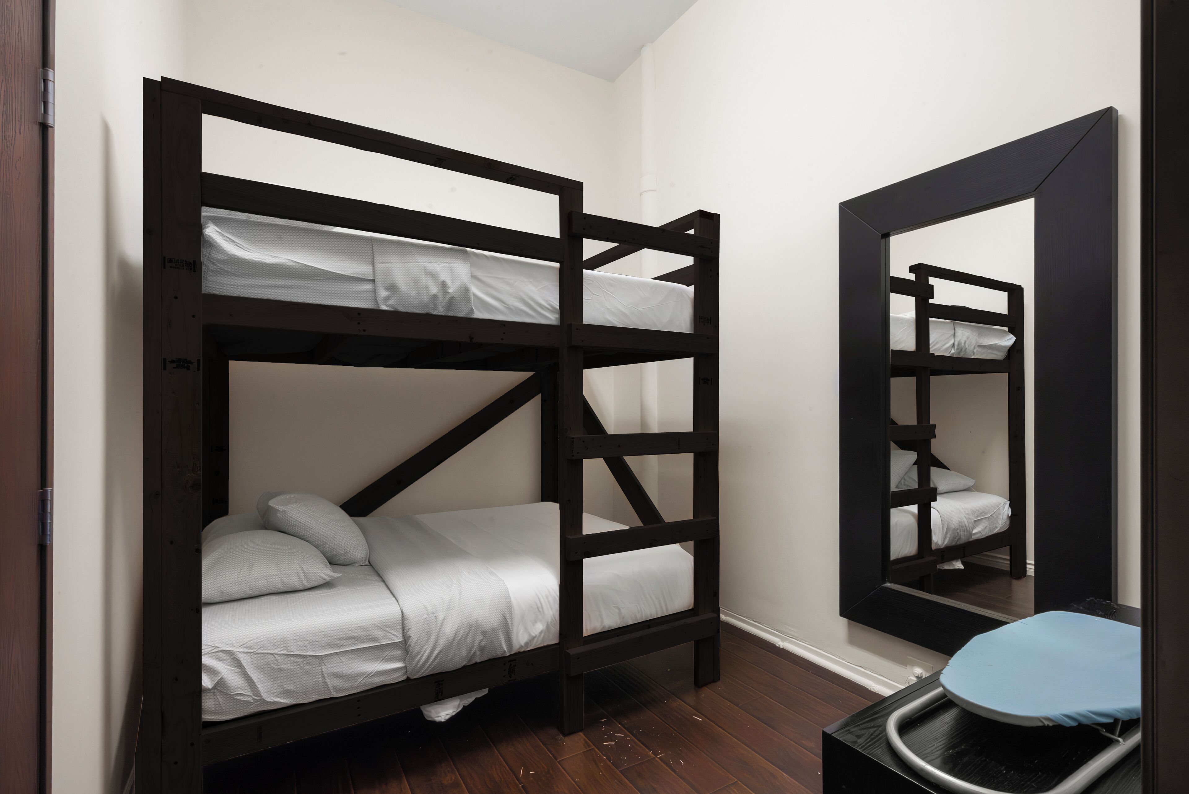 A bunk bed room with a mirror reflecting the bed and a small table with a chair.