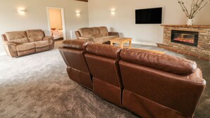 Un salon avec un canapé en cuir marron, une table basse en bois, une cheminée et un téléviseur à écran plat fixé au mur.