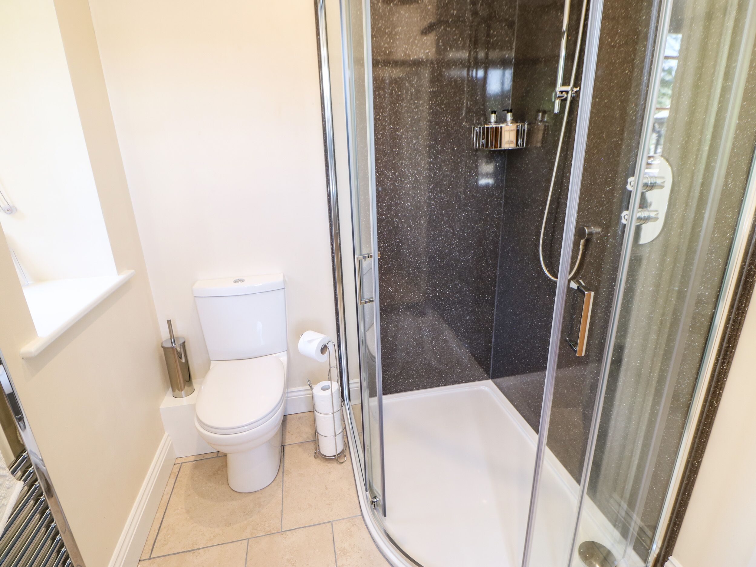 A bathroom with a toilet, a glass shower enclosure, and a toilet paper holder.