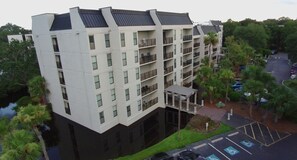 A multi-story hotel with balconies, a parking area, and surrounding greenery. - BEACH CONDO STEPS FROM COLIGNY PLAZA — Your Perfect Hilton Head Family Escape<br><br>Wake up to lagoon views and fall asleep to ocean breezes. This charming 3-bedroom beachside condo puts you just steps from Coligny Plaza and direct beach access. (Hilton Head Island)