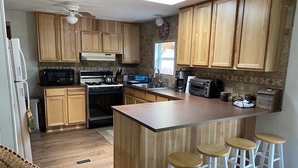 A kitchen with wooden cabinets, a central island with stools, a microwave, stove, oven, and a toaster.