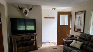 A living room with a television on a wooden stand, a black leather sofa, a door, and a wall-mounted picture.