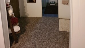 A hallway with a wooden door, a mirror, a towel rack, and a carpeted floor.