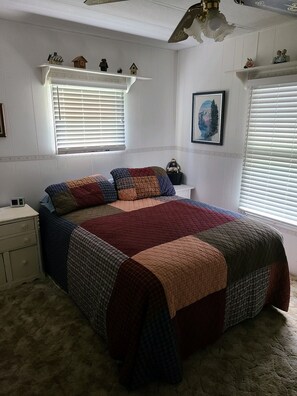 Une chambre à coucher avec un grand lit, une table de chevet, une commode et une fenêtre avec des stores.