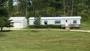 A single-story building with a white exterior and blue shutters, surrounded by a grassy area and trees.
