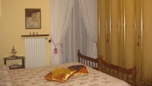 Une chambre à coucher comprenant un lit, un radiateur, une table de chevet, une lampe, un miroir et une armoire.