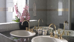 Une salle de bain avec deux vasques, des robinets dorés et une composition florale décorative à base d’orchidées.