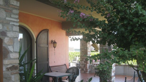 Un espace extérieur aménagé en terrasse, avec une table et des chaises, un mur en pierre et une pergola couverte de plantes grimpantes.