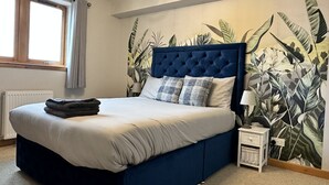 Ein Schlafzimmer mit einem großen Bett, einem Fenster, einem Heizkörper, einem Nachttisch und einer Wand mit tropischem Blattmuster.