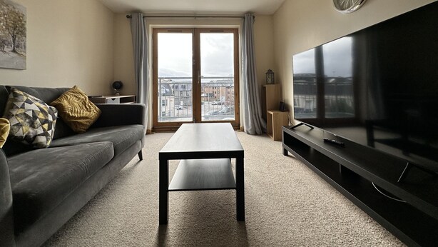 Ein modernes Wohnzimmer mit Sofa, Couchtisch, Flachbildfernseher und einem großen Fenster mit Blick auf die Stadt.