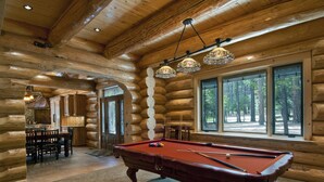 A log cabin interior with a pool table, dining area, and large windows offering a view of the forest. - (67) El Capitan (3 Bedrooms Only) at The Redwoods In Yosemite (Yosemite National Park)