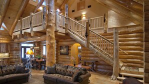 A log cabin interior with a central staircase, a dining area, and a cozy seating arrangement. - (67) El Capitan (3 Bedrooms Only) at The Redwoods In Yosemite (Yosemite National Park)