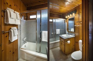 Un baño de cabaña de madera con ducha de vidrio, bañera y lavabo con espejo.