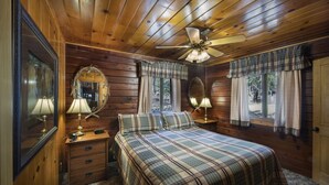 A wooden cabin bedroom with a plaid bedspread, two bedside lamps, a ceiling fan, and a large mirror. - (72) Sequoia (1 Bedroom Only) (Yosemite National Park)
