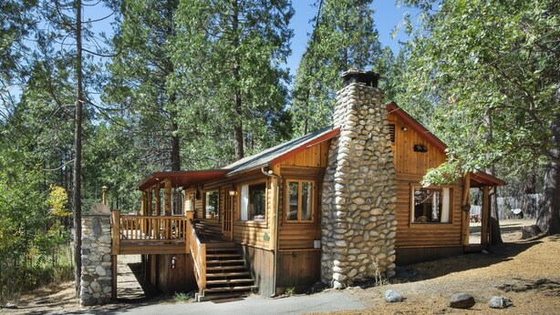 A rustic cabin with a stone chimney, wooden deck, and a staircase leading to the entrance. - (72) Sequoia (1 Bedroom Only) (Yosemite National Park)