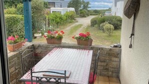 Une terrasse couverte avec une table et des chaises, des plantes en pot et une vue sur les environs.