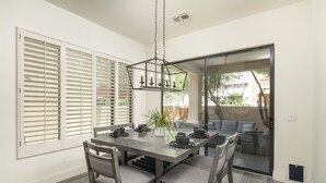 A dining area with a table set for four, surrounded by chairs, a hanging light fixture, and a sliding glass door leading to an outdoor space. - Modern Spacious 2 Master Bedroom Cal King with Loft & Pool Sleeps 6 (Chandler)