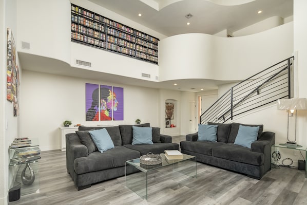 A spacious living area with two grey sofas, a glass coffee table, and a bookshelf filled with books.