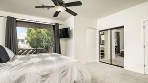 A bedroom with a bed, a ceiling fan, a TV, and a sliding glass door leading to a balcony. - Modern Spacious 2 Master Bedroom Cal King with Loft & Pool Sleeps 6 (Chandler)