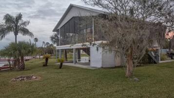 A modern two-story house with a large balcony, surrounded by a well-maintained lawn and palm trees.