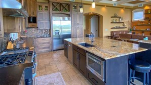 A modern kitchen with granite countertops, stainless steel appliances, and a central island with bar stools. - Luxury Construction, Heated Pool on Canal, 3 Minute Walk to sugar sand of FMB! (Fort Myers Beach)
