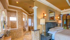A spacious bedroom with a large bed, a nightstand, a mirror, and a stone accent wall. - Luxury Construction, Heated Pool on Canal, 3 Minute Walk to sugar sand of FMB! (Fort Myers Beach)