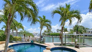 A swimming pool with a hot tub, surrounded by palm trees and a marina in the background. - Luxury Construction, Heated Pool on Canal, 3 Minute Walk to sugar sand of FMB! (Fort Myers Beach)