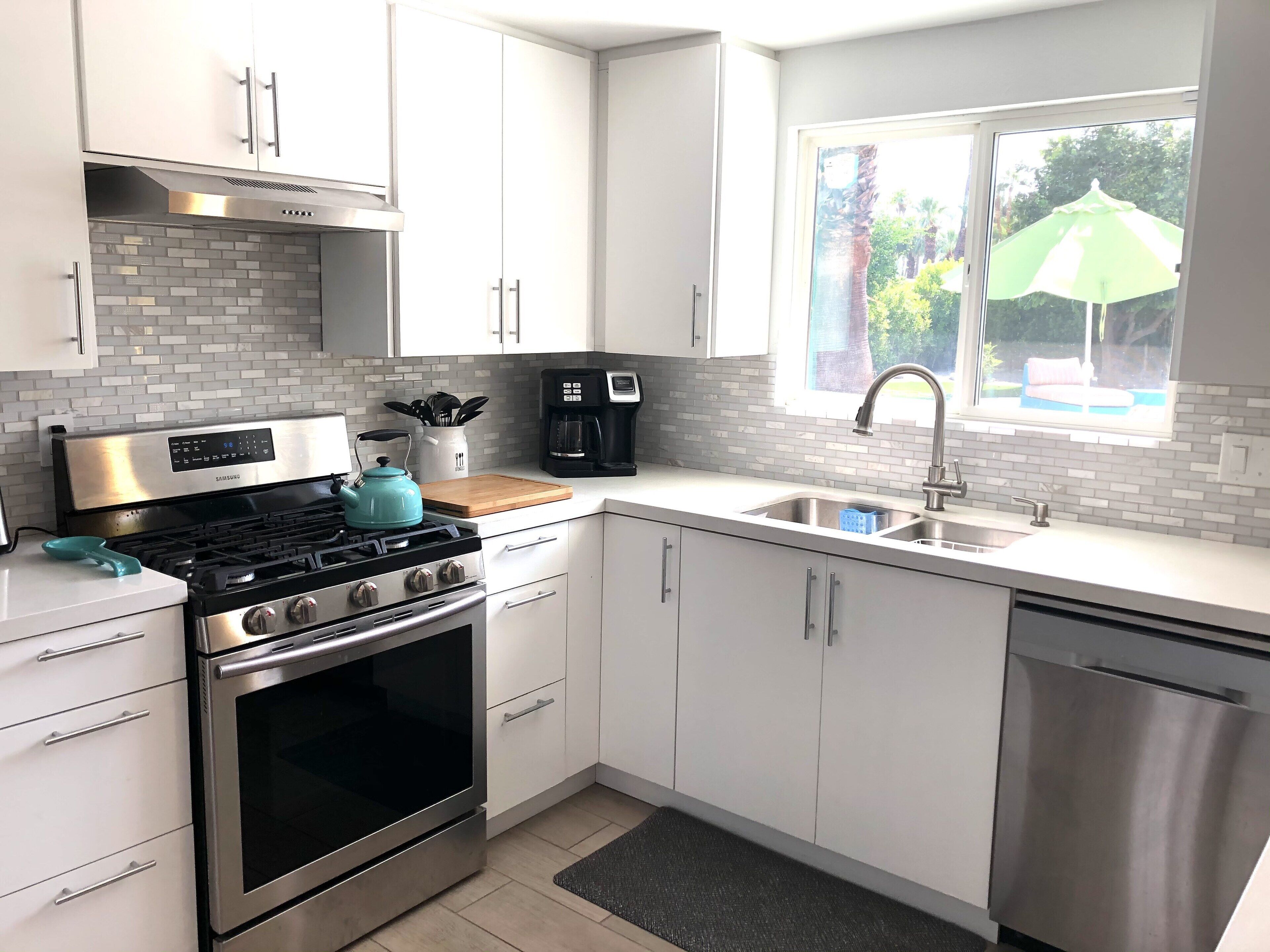 A modern kitchen with white cabinets, stainless steel appliances, and a window with an umbrella.