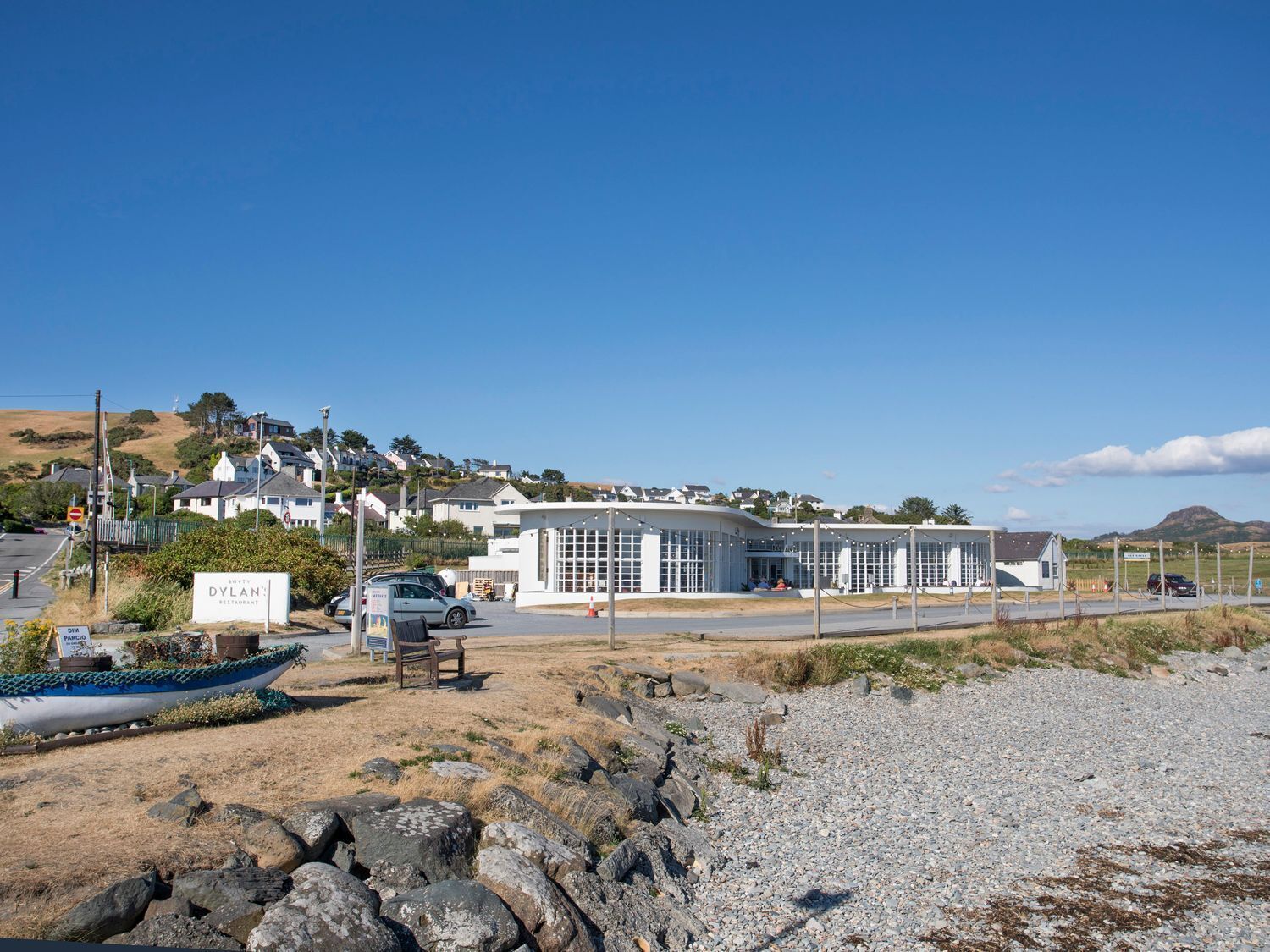 A coastal building with a modern design, a parking area, and a rocky foreground.