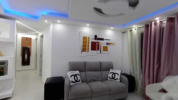 A modern living room with a grey sofa, two black speakers, and a white armchair. - Luxurious Apartment 4to level with security camera (Santo Domingo Norte)