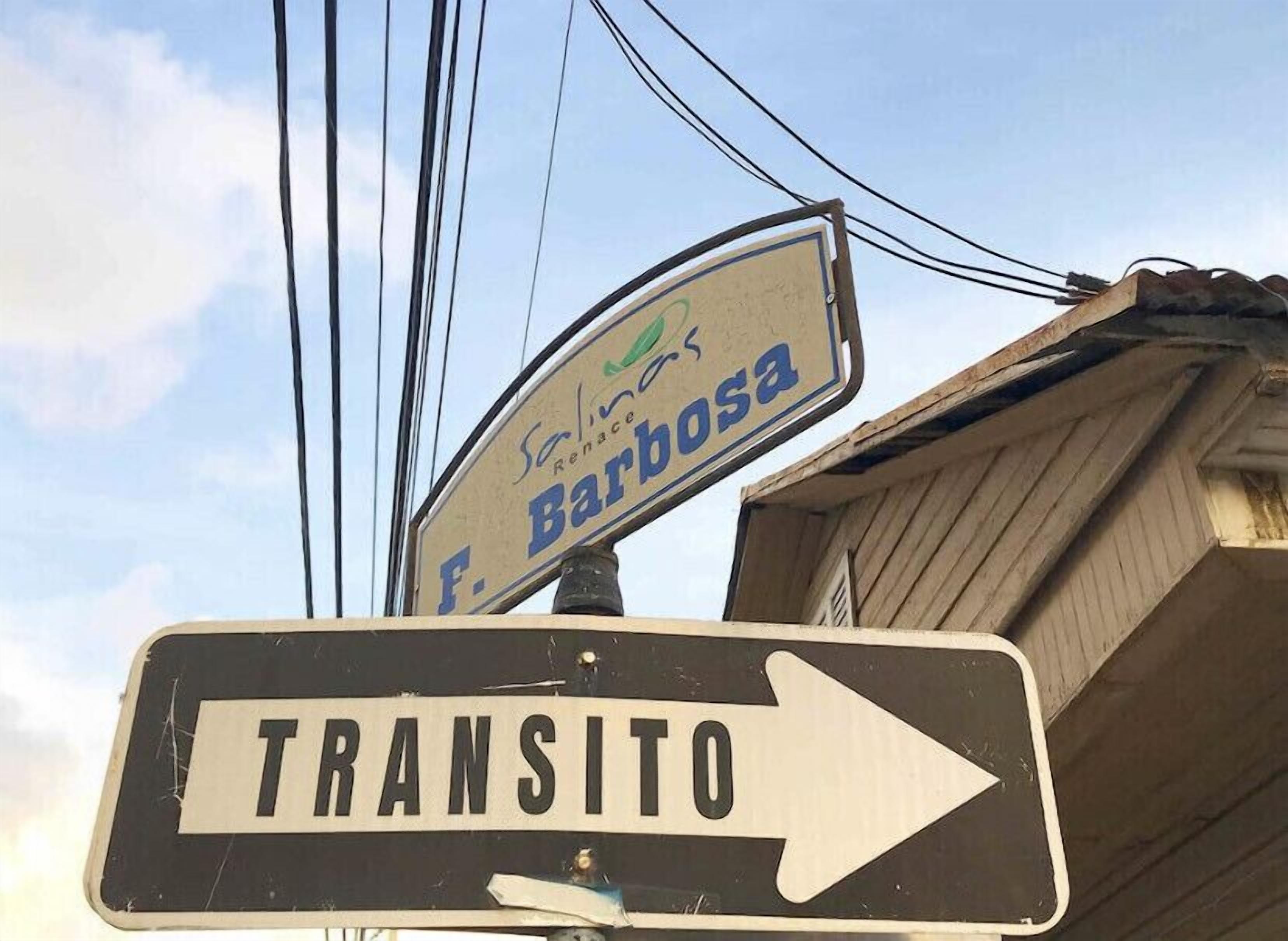 Una señal de calle con la inscripción 'F. Barbosa' y una señal de indicaciones de transporte.