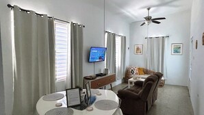 A living room with a round table, a sofa, a television, and ceiling fans.