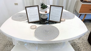 A round table with a white tablecloth, two framed welcome signs, a small potted plant, and three coasters.