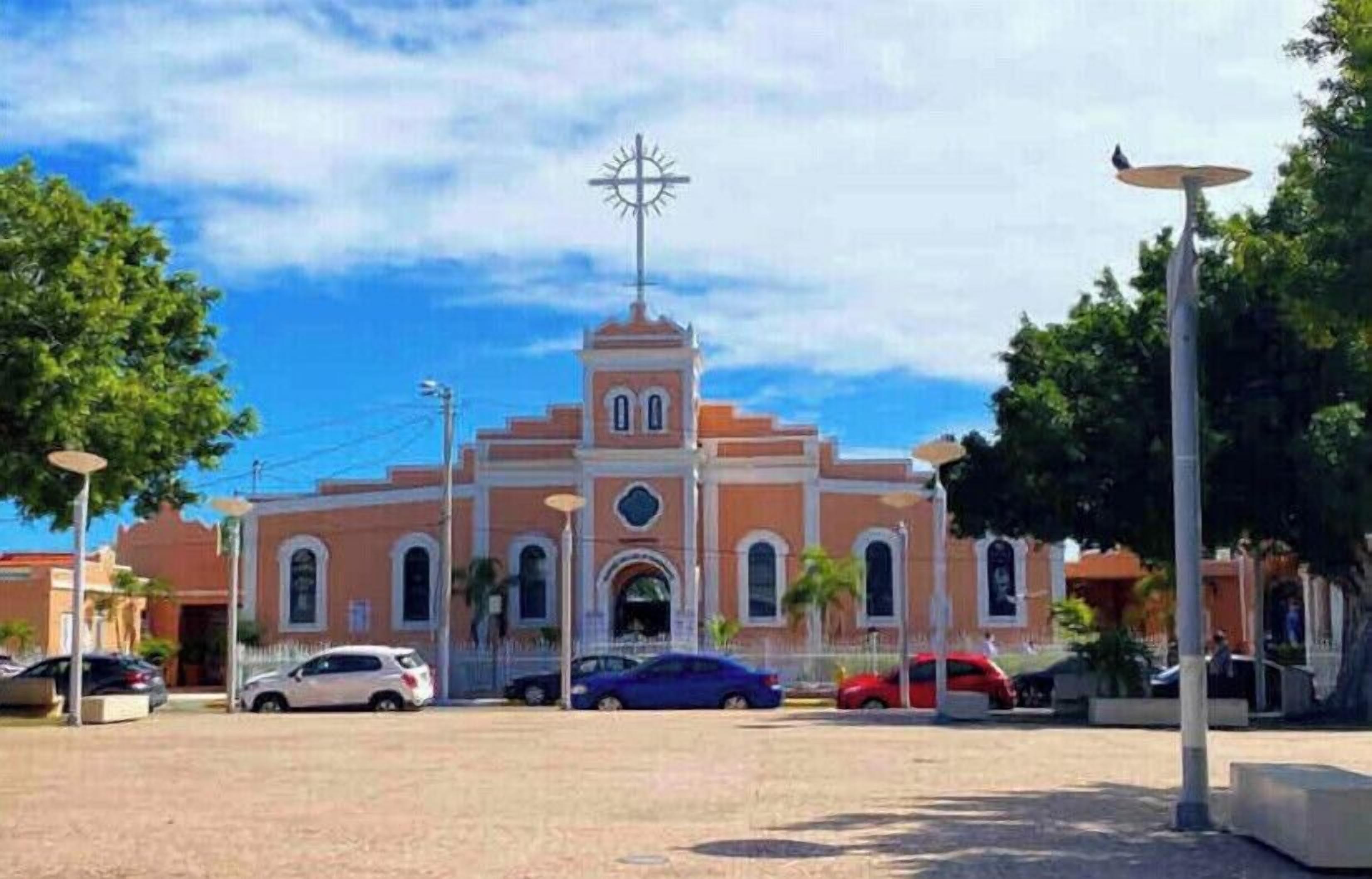 A church with a cross on top, surrounded by trees and parked cars.