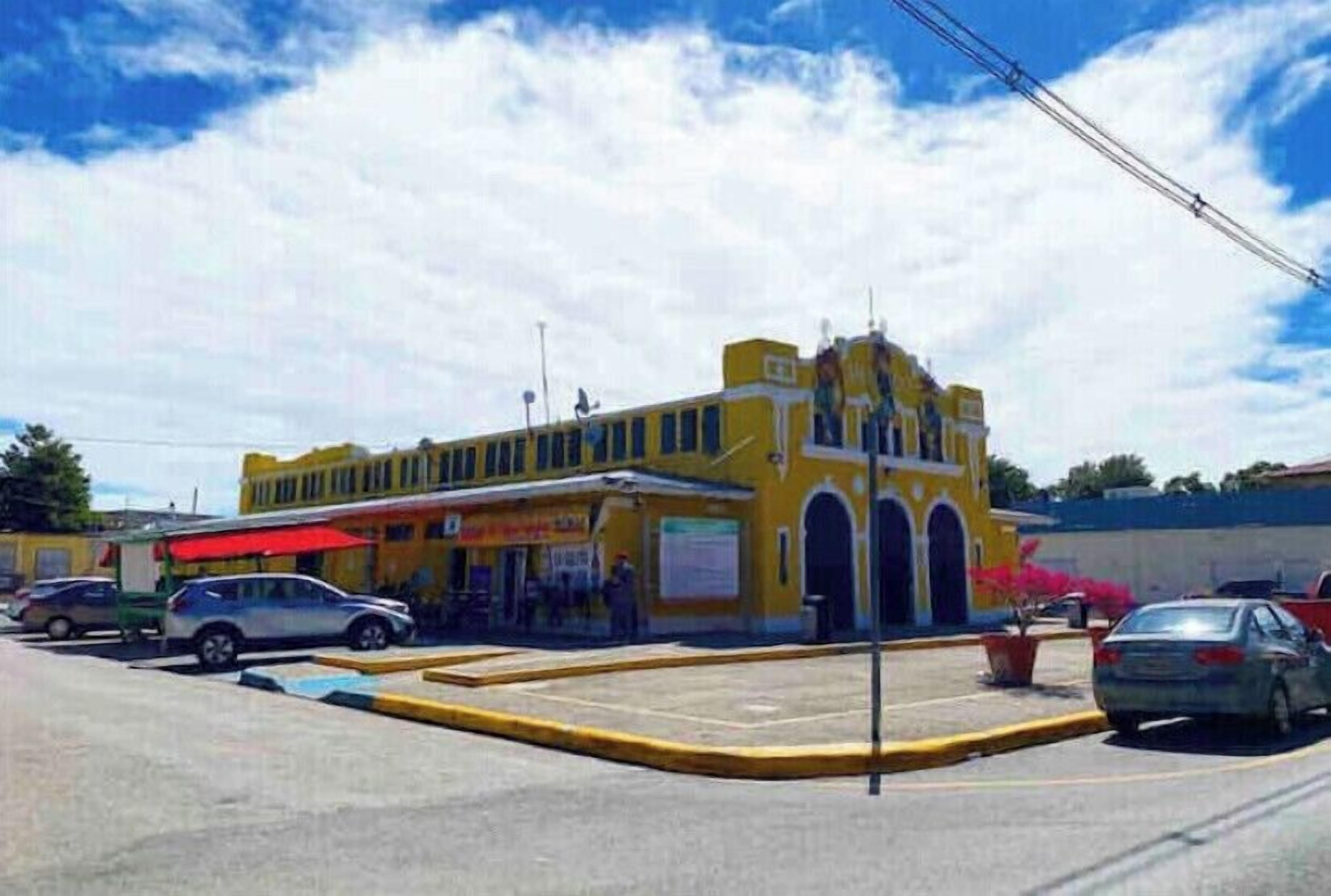 A yellow building with a red awning, a parking lot, and a few cars.